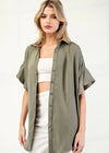Woman wearing an olive green button-up shirt over a white top and pants on a white background