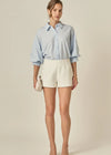 Woman wearing a light blue striped shirt and white shorts on a beige background