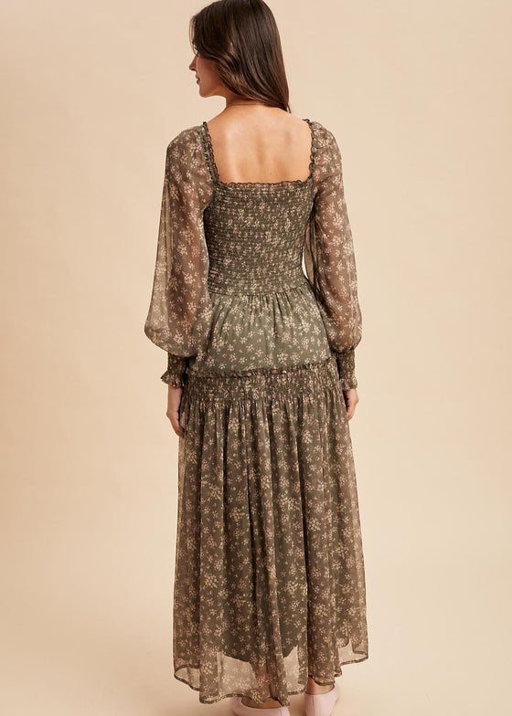 Woman wearing a long, patterned dress with sheer sleeves on a beige background