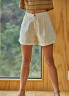 Person wearing beige shorts standing in a room with wooden walls and a window.