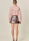 Person wearing a striped shirt and metallic skirt on a beige background