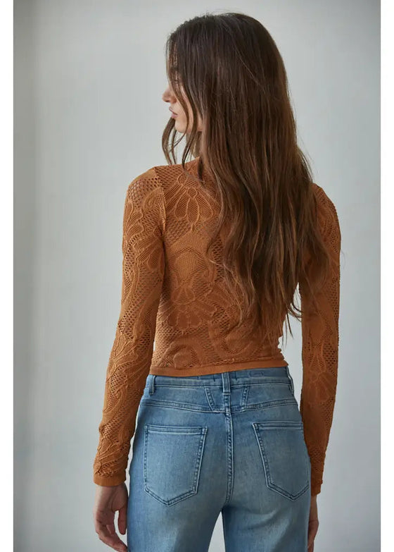 Woman wearing a brown lace top and blue jeans against a plain background