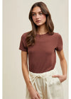 Woman wearing a brown t-shirt and beige pants against a neutral background