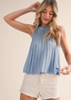 Woman wearing a light blue sleeveless top and white shorts on a beige background
