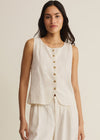 Woman wearing a sleeveless beige top with gold buttons on a plain background