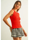Woman wearing a red sleeveless top and checkered skirt on a plain background
