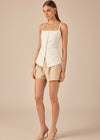 Woman wearing a white sleeveless top and beige shorts on a beige background