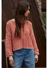 Woman wearing a red and white striped sweater and blue jeans standing against a wooden wall.