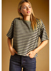 A woman wearing a short-sleeve crewneck t-shirt with thin horizontal black stripes on a beige background, paired with dark blue jeans, set against a solid warm brown studio backdrop.