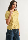 Woman wearing a yellow lace top and blue jeans on a white background