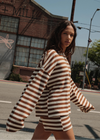 A woman walking on a city street wearing a brown and cream striped oversized long-sleeve top and matching shorts.