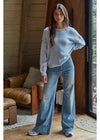 Woman wearing a light blue sweater and jeans in a cozy room with wooden walls and furniture.