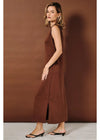 A woman modeling a sleeveless, brown maxi dress with a side slit, standing against a solid brown studio backdrop.