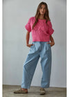 Woman wearing a pink knitted sweater and blue jeans against a plain background