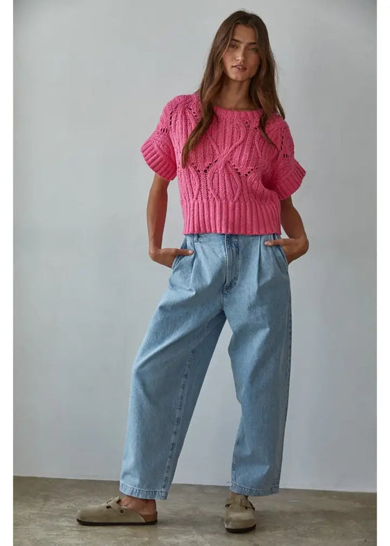 Woman wearing a pink knitted sweater and blue jeans against a plain background