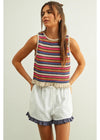 Woman wearing a colorful striped sleeveless top and white shorts on a light background