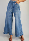 Blue jeans with ruffled cuffs worn by a person on a plain background