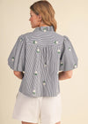 Woman wearing a blue and white striped blouse with floral embroidery on a beige background