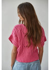 Woman wearing a pink knitted top against a plain background