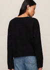 Person wearing a black sweater and blue jeans on a plain background