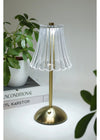 Small table lamp with pleated design on a white surface with books and a plant in the background.