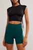 Person wearing a black crop top and teal shorts on a plain background