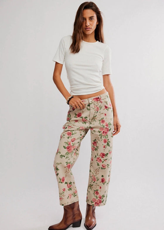 Woman wearing a white t-shirt and floral pants on a plain background