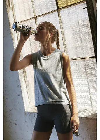 Woman in athletic wear drinking from a water bottle indoors.
