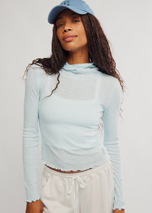  Woman wearing a light blue long-sleeve top and beige pants against a white background