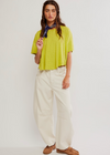 Woman wearing a bright yellow top and white pants against a plain background