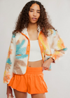 Woman wearing a colorful jacket and orange shorts against a white background