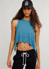 Woman wearing a blue sleeveless top and black pants with a white drawstring against a plain background