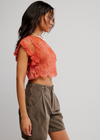 Woman wearing an orange lace top and brown shorts on a plain background
