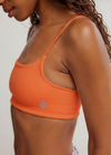 Person wearing an orange sports bra with a brand logo on a plain background