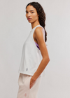 Woman wearing a white sleeveless top with a small logo on a plain background