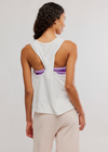 Woman wearing a white tank top with open back and purple accents on a plain background