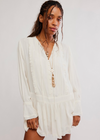 A woman wearing a white long-sleeve blouse with ruffle trim and a button-front bodice, photographed against a plain light gray studio background.