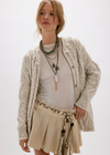Woman wearing a beige knitted cardigan over a white shirt with a beige skirt on a white background