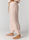 A person wearing light blush pink cable-knit lounge pants with a drawstring waist and side pocket, shown from the waist down against a plain light gray studio background.