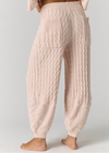 A person shown from the back wearing light blush pink cable-knit harem-style pants with a matching knit top partially visible, standing against a plain light gray studio background.