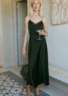 Woman in a dark green slip dress holding a glass in an elegant room.