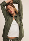 Woman wearing a green jacket and pants with a white top against a beige background