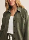 Person wearing an olive green jacket over a white top on a plain background
