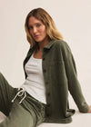 Woman wearing an olive green jacket and pants sitting on a white surface.
