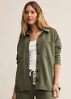 Woman wearing an olive green button-up shirt over a white top and green pants on a beige background
