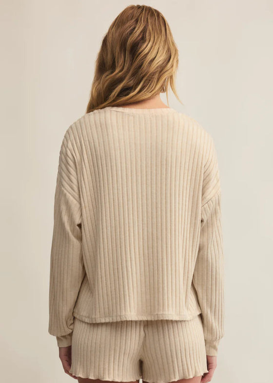 Woman wearing a beige ribbed sweater and shorts set on a plain background