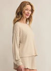Woman wearing a beige ribbed sweater and skirt set against a plain background
