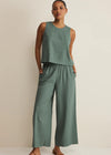 Woman wearing a green sleeveless top and wide-leg pants against a beige background