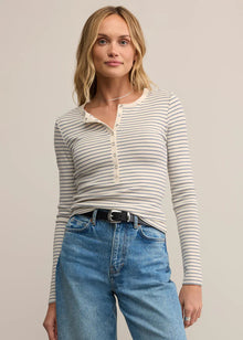  Woman wearing a striped long-sleeve top and blue jeans on a plain background