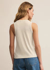 Woman wearing a beige sleeveless top and blue jeans on a plain background